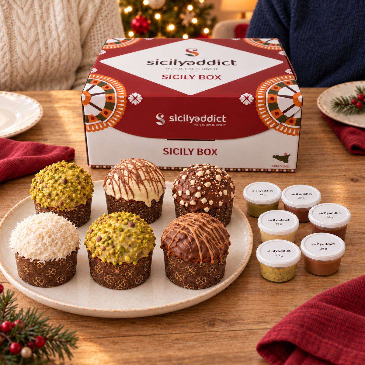 Box di 6 panettoncini assortiti su una tavola natalizia, con persone sullo sfondo.