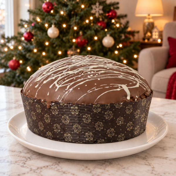 Panettone Ciokonocciola SicilyAddict intero con copertura al cioccolato al latte e variegatura chiara, su piatto bianco in ambiente natalizio.