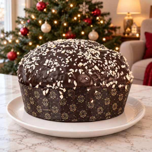 Panettone ai Tre Cioccolati intero, con copertura scura e scaglie bianche, su piatto in ambiente natalizio.