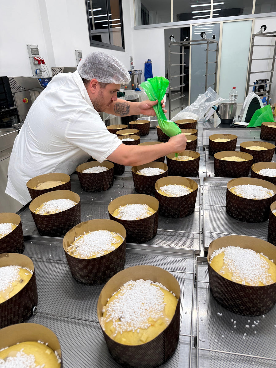Pasticcere che stende la glassa con la sac à poche su ogni panettone